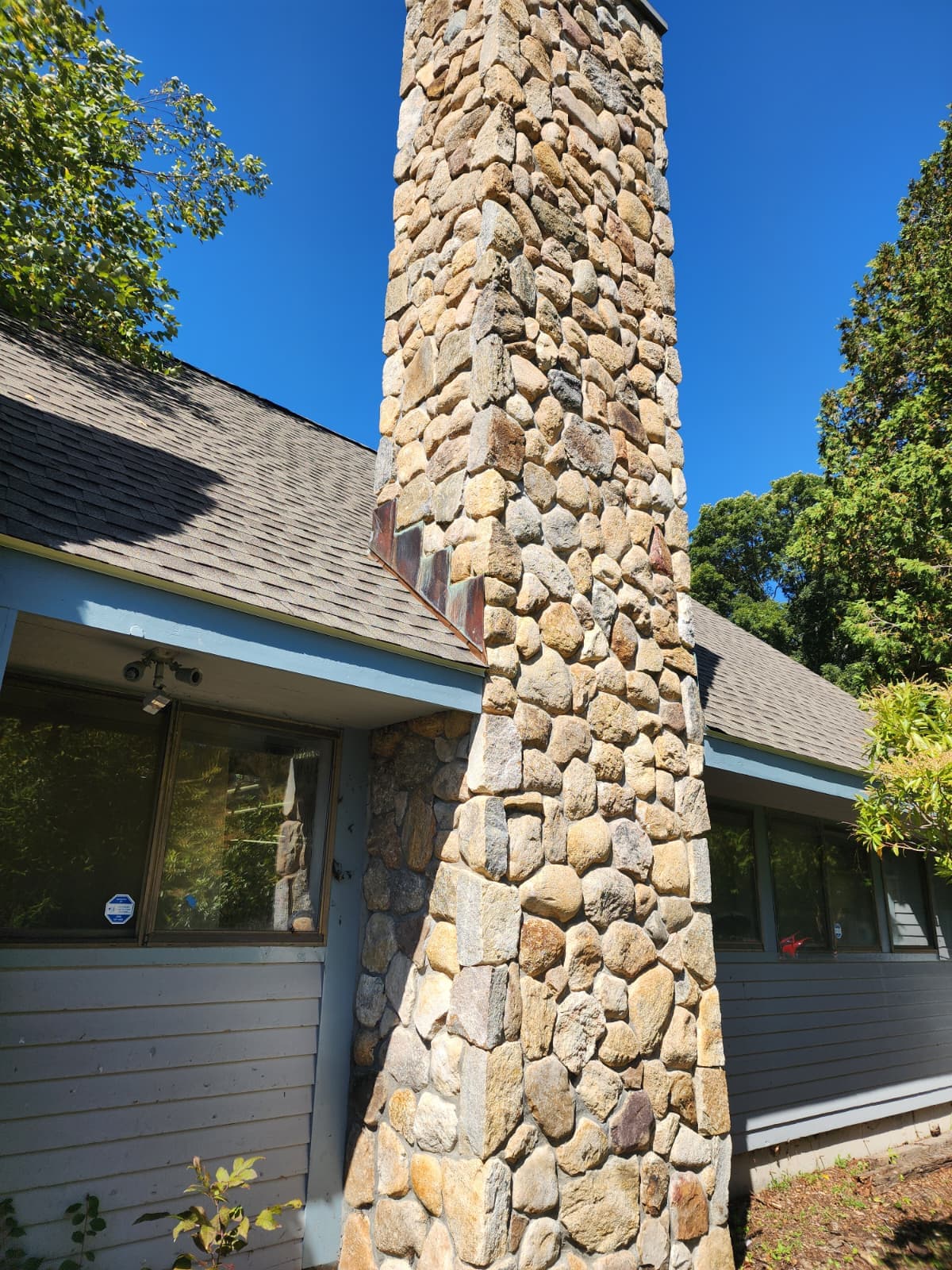 Fieldstone chimney veneer — Connecticut Full-height natural fieldstone chimney veneer against a blue sky